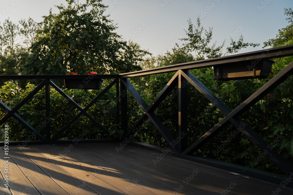 Obraz premium Wooden terrace with decorative railing and garden view, outdoor patio architecture with wooden flooring, greenery, and sunlight shadows for home and landscaping design inspiration
