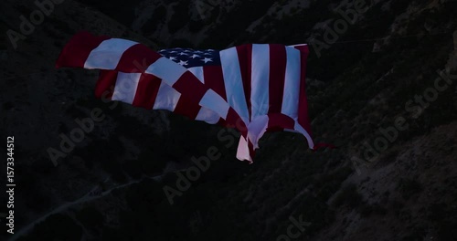 Shadow over epic, majestic American flag flowing in rocky mountains - drone shot