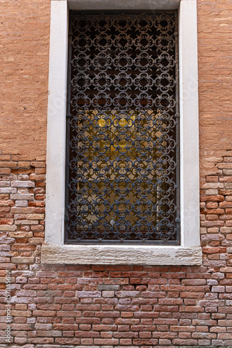 A detailed close-up of a Venetian window with ornate wrought iron, flower pots, and weathered stone and brickwork.