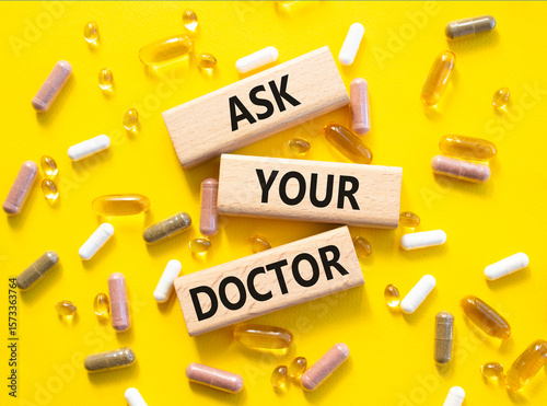 Ask Your Doctor symbol. Concept word Ask Your Doctor on wooden blocks. Beautiful yellow background with pills. Medicine and Ask Your Doctor concept. Copy space