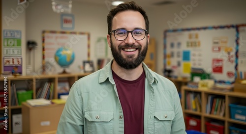 Smiling Male Teacher in Light Green Shirt Inside a Bright and Colorful Classroom