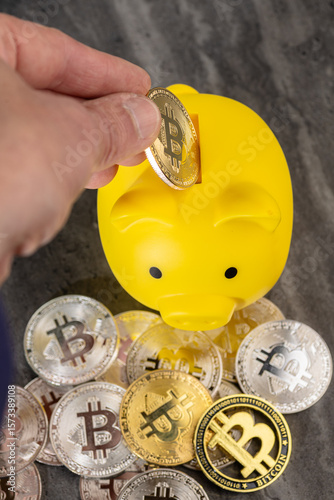 Hand Investing Bitcoin Coin into Yellow Piggy Bank Representing Cryptocurrency Savings