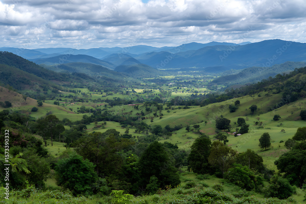 Fototapeta premium Lush Green Rolling Hills Valley Landscape Scenic View Distant Blue Mountains Cloudy Sky Rural Farmland