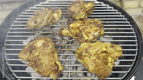 Closeup of pieces of chicken, cooking on a grate over hot charcoal in an outdoor barbecue grill.