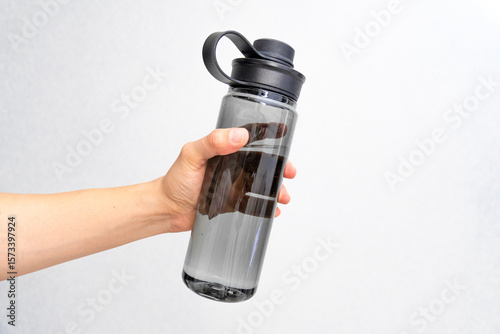 Photograph of a Caucasian person's hand holding a closed transparent bottle of water