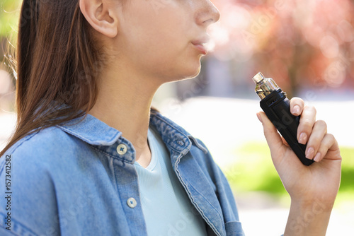 Young woman using electronic smoking device outdoors, closeup