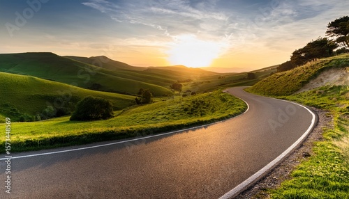 a winding road leading into the distance with green hills and trees on both sides of it the sun is setting in the background
