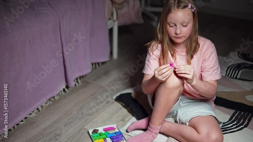 Caucasian girl sits on the floor in her room in the evening and creating sculpture from plasticine. Slow motion of female kid molding modeling clay in hands to make funny figure. Educational game
