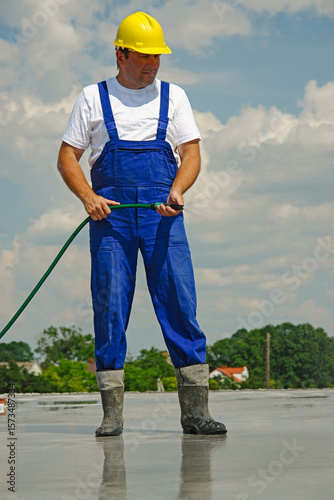 Worker Spraying Water to Cool a Concrete Surface on a Sunny Day