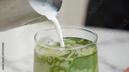 Pouring creamy milk into a glass of vibrant matcha tea for a delicious and visually appealing beverage