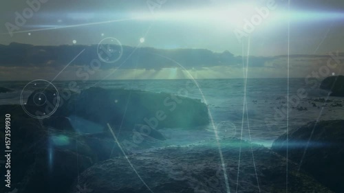 Rising sun peeking over horizon causing waves lapping rocks while HUD arcs and lens flares scanning