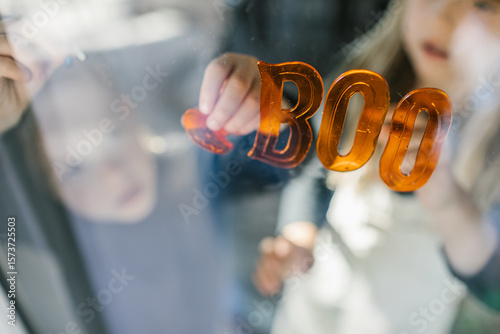 Siblings decorating window with boo sign for halloween