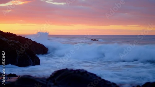 Coastal Sunrise Symphony: The sun's golden embrace paints the sky, illuminating the untamed dance of waves crashing against rugged coastal rocks in a serene seaside scene.