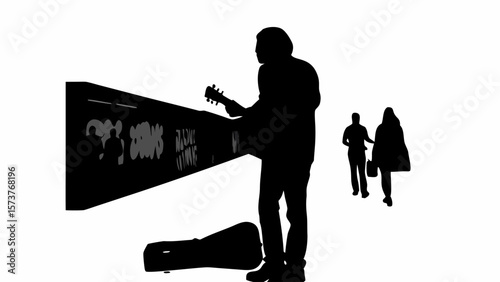 Silhouette of a street musician playing guitar near a graffiti wall with people walking in the background