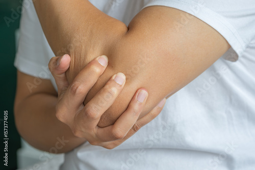 Obraz na plátně An Asian man clutches their elbow in apparent discomfort, possibly due to inflammation or strain