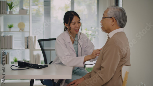 A caring female doctor in a lab coat uses a stethoscope to examine an elderly male patient in a bright medical clinic. The scene highlights patient care, medical examination, and support for seniors.