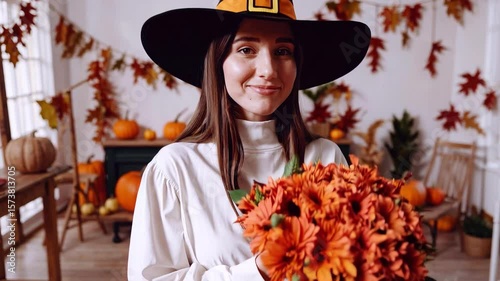 Woman in witch hat holding autumn flowers in festive fall decorated room
