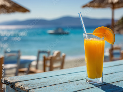 Fototapeta Naklejka Na Ścianę i Meble -  A glass of fresh orange juice on the table at a summer beach bar with a beautiful view of the blue lagoon in Greece. 