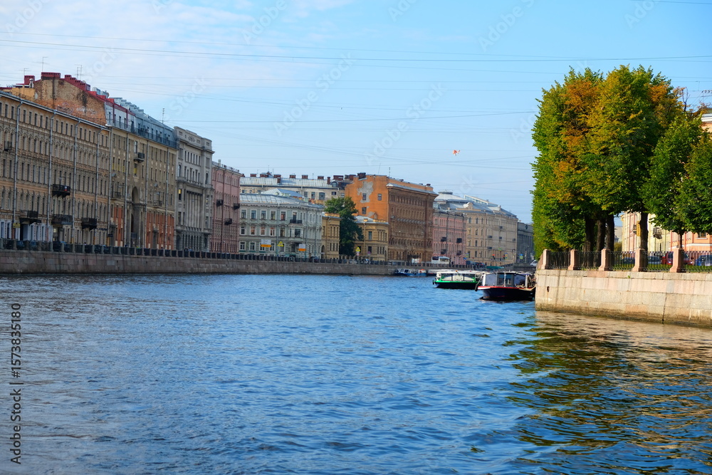 Obraz premium A vibrant boat tour through St. Petersburg's canals, showcasing historical architecture, bridges, and city life under a clear sky