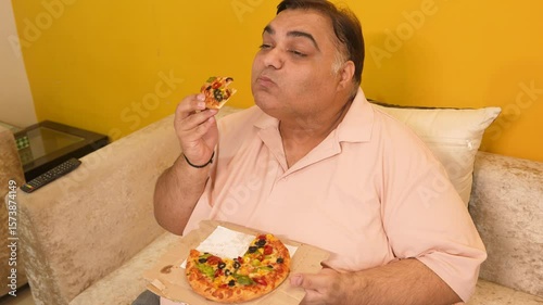 Hungary overweight fat indian man eating cheese pizza. Plus size guy enjoy fatty junk food. Obese male taking a bite of high calorie meal. Obesity and weight gain.4k