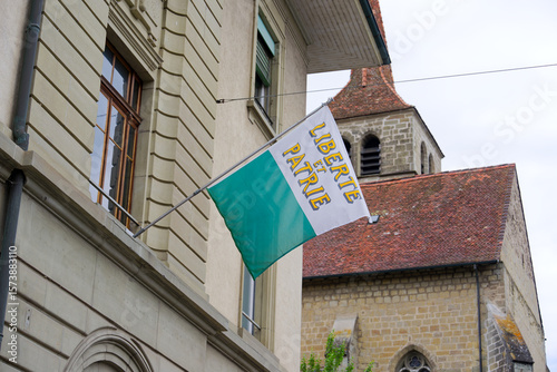 Cityscape of Swiss city of Payerne with flag of canton of Vaud outside of police station on a cloudy spring day. Photo taken June 6th, 2025, Payerne, Switzerland.