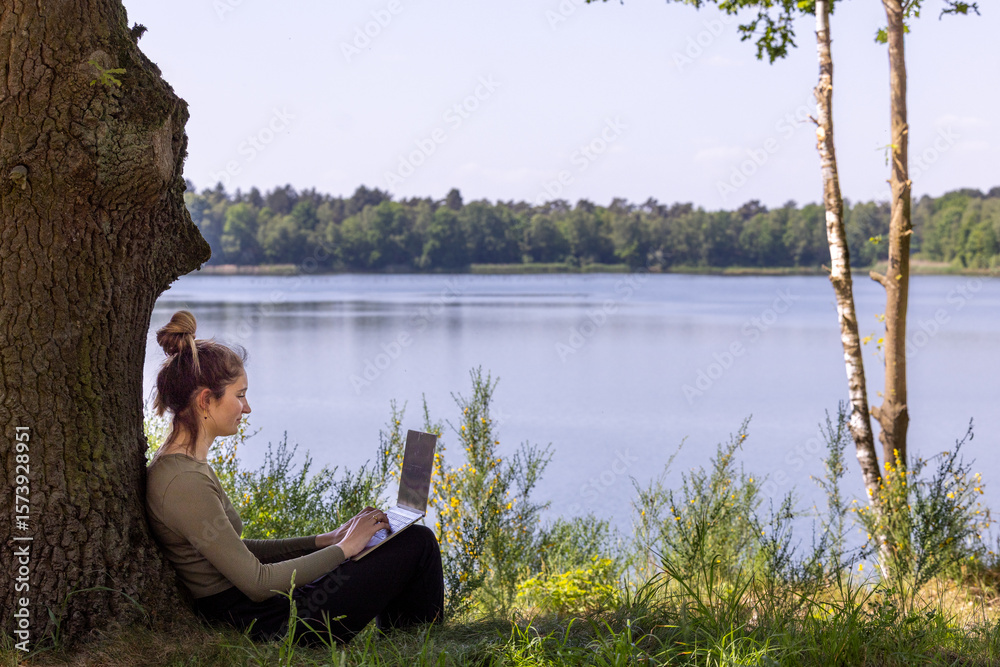 Fototapeta premium A woman enjoys a wonderfully productive day working on her laptop while relaxing by a peaceful lakeside