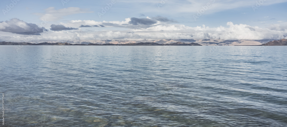 Fototapeta premium Panorama landscape of Lake Karakul in the Pamir mountains in the Tien Shan against the background of high snowy rocky peaks with clouds, morning panorama of the lake for the background