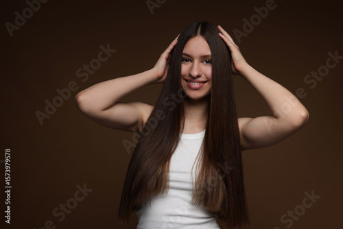 Portrait of smiling teenage girl with healthy long hair on brown background