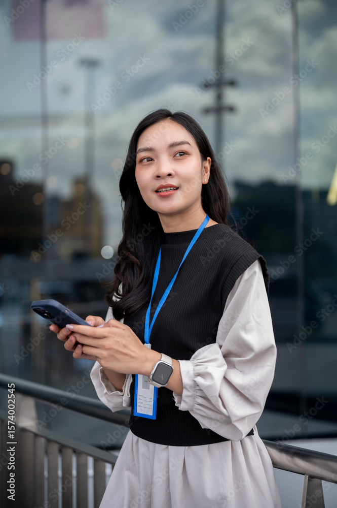 Female office worker or event staff holding looking away from phone while standing leans on railing. Female office worker or event staff holding looking away from phone while standing leans on railing.