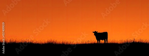 Artistic silhouette of a cow standing still against an orange sunset sky.