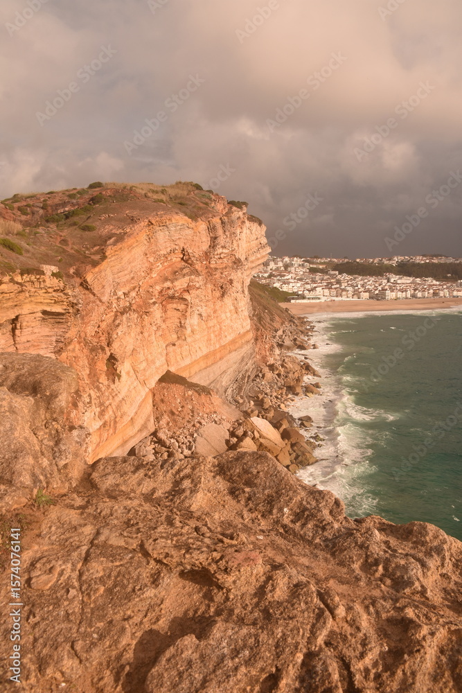 Obraz premium Dramatic sea cliffs bathed in golden light, overlooking São Lourenço Beach and the town of Ericeira, Portugal—famous for its surfing and rugged Atlantic coastline.