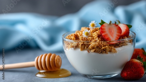 Yogurt and granola bowl with strawberries, a honey dipper on the side