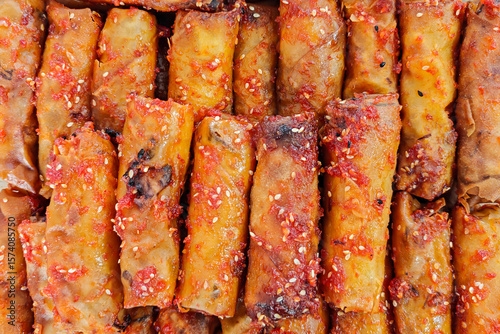 Close-up of spicy fried spring rolls coated with chili sauce and sesame seeds – a popular traditional Malaysian snack that's crispy and flavorful.