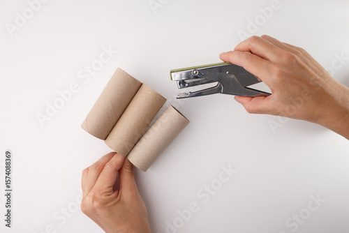 Bilde på lerret hands-on DIY moment in progress, hand is holding three empty cardboard toilet paper rolls, stapler staple rolls together