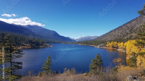 Serene mountain lake view with vibrant autumn foliage, clear blue water, and majestic peaks under a bright sky