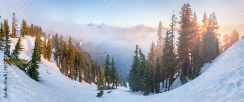 Snow covered rim of Crater Lake and Wizzard Island in Crater Lake National Park, Oregon. A panoramic cliff-side overview of deep blue Crater Lake, surrounded by the rugged lake rim, on a calm Spring 