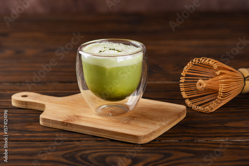 Pistachio matcha latte tea with whipped milk in a glass on a wooden board with bamboo chasen.