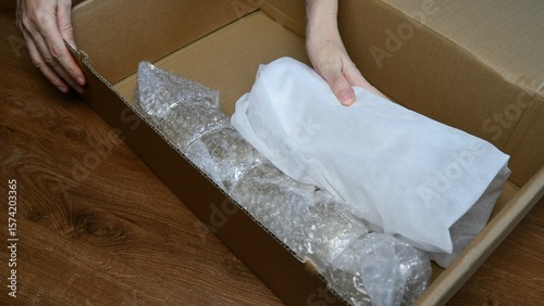 Packing up fragile tableware into plastic bubble wrapping inside cardboard box
