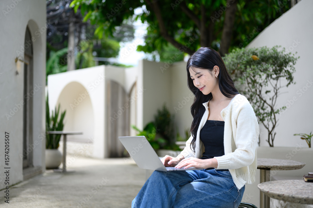 Obraz premium Freelancer enjoying remote work at a quiet outdoor cafe with green plants and natural light