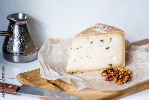 A piece of fresh, aged, natural farm cheese with walnuts on parchment on a wooden board. The quality of farm-fresh agricultural products.
