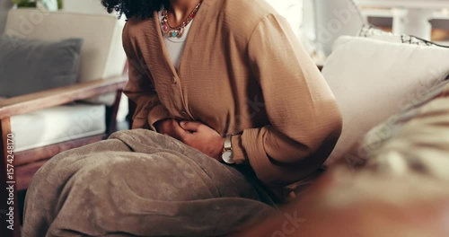 Stomach ache, hands and woman on sofa in home with menstruation cramps, IBS or constipation. Sick, tummy pain and female person with bloating for abdominal problem in living room at apartment.