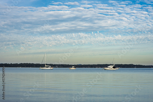 View from Coochiemudlo Island across calm waters to Macleay Island, featuring white fluffy clouds against a blue sky, and three moored boats. Queensland, Australia 