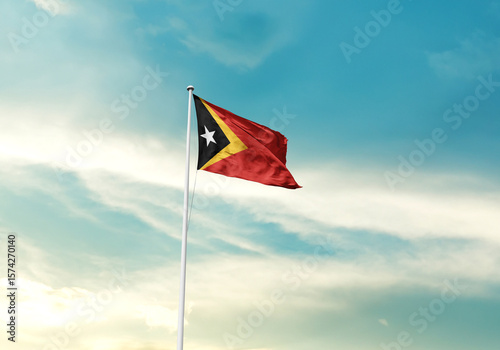 East Timor flag is waving on a tall flagpole among the clouds. East Timor national flag for independence day.