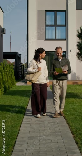 A husband and wife are looking at a booklet with a design project of a house while walking in the backyard