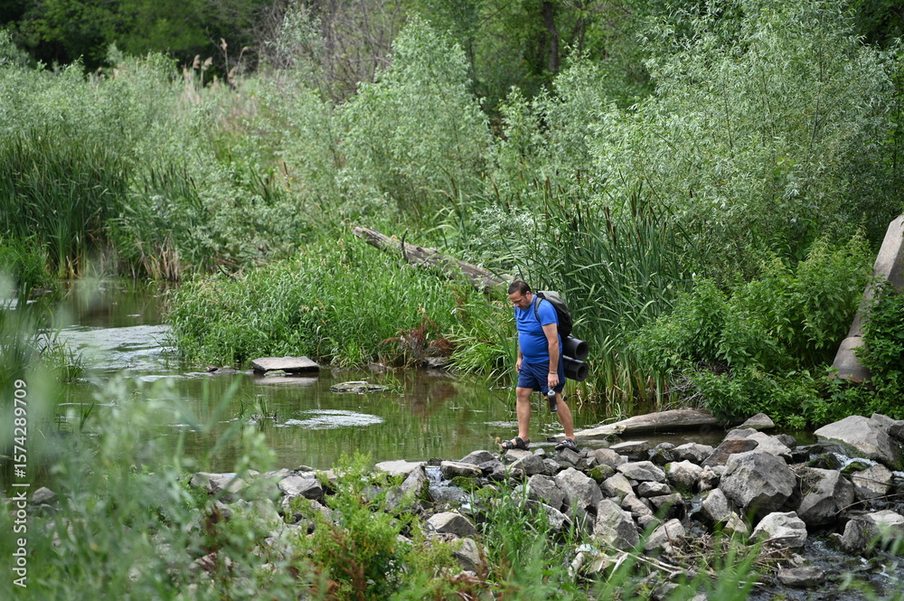 Obraz premium A man crosses a river on rocks with a backpack.