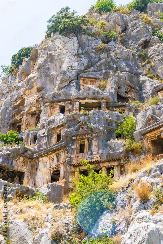 Naklejka premium Demre, Turkey - June 14, 2025:View of the ancient Lycian necropolis and Roman amphitheater in the ruins of Myra, located in Demre, Antalya Province, Turkey.