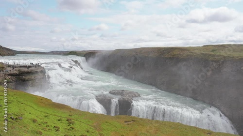 Outdoors, huge waterfall view, Iceland nature landscape, serenity view of the waterfall, melting glacier water flow, tourist places and paths, green rocky terrain.