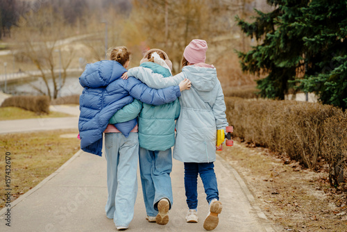Teen girls walk together, hugging shoulders, each holding a skateboard. Jackets, jeans, sneakers show winter street style. Outdoor friendship, movement, balance, youth bonding, lifestyle and freedom