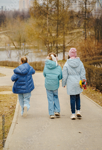 Teen girls ride skateboards on city path in winter park. Jackets and jeans reflect urban youth style. Street sport improves balance, movement, coordination, friendship and outdoor fun for kids