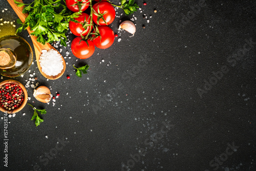Food background with fresh vegetables, herbs and spices on black.